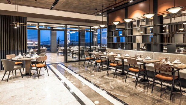 Un restaurante moderno con suelo de mármol, varias mesas y sillas para comer, e iluminación colgante.