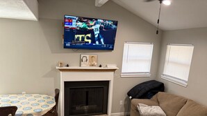 Ett vardagsrum med en öppen spis, en tv som är monterad på väggen, ett matbord med stolar och en soffa.