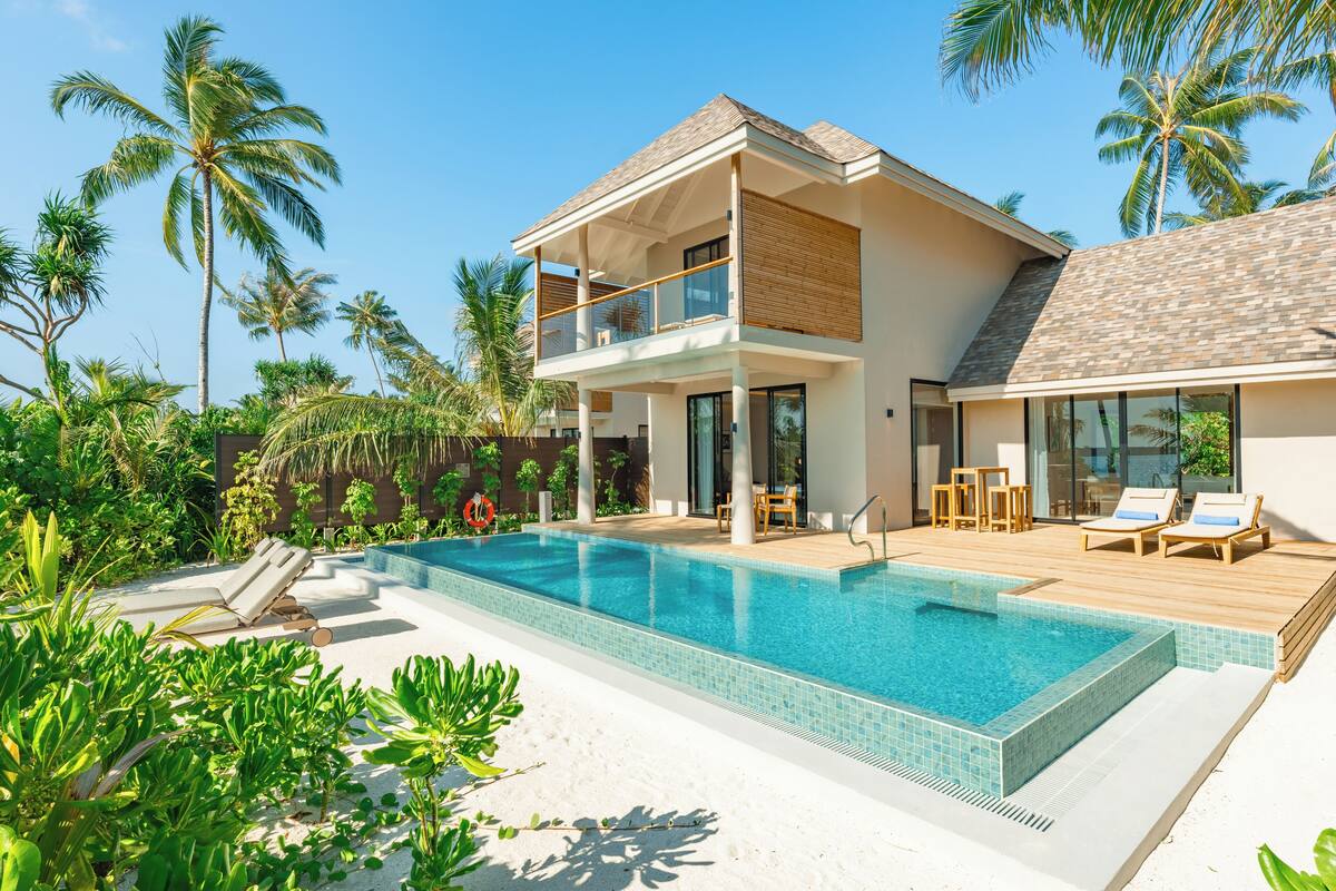 A two-story modern house with a swimming pool, surrounded by tropical vegetation.