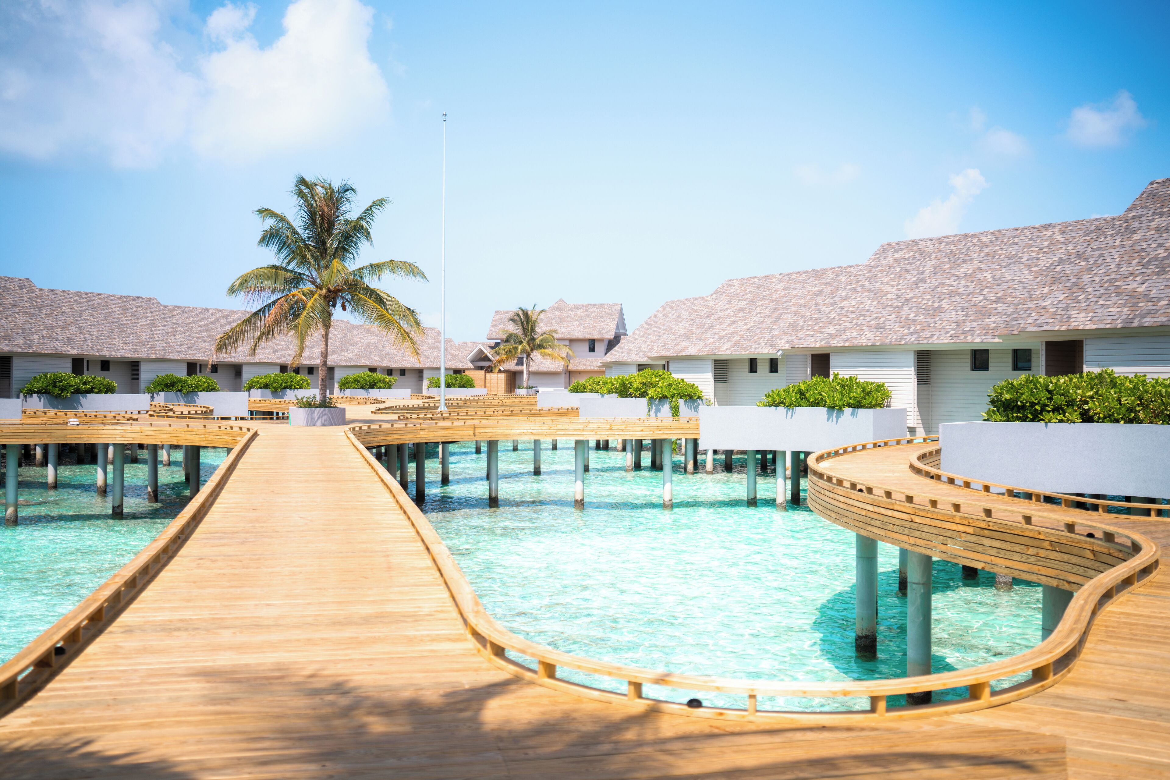 A resort with overwater bungalows connected by wooden walkways over clear blue water.