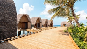 Une terrasse en bois mène à des bungalows sur pilotis offrant une vue dégagée sur la mer.