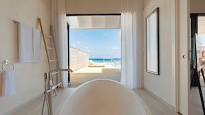 Une salle de bain moderne avec une grande baignoire, une échelle en bois et une vue sur la plage par une porte ouverte.