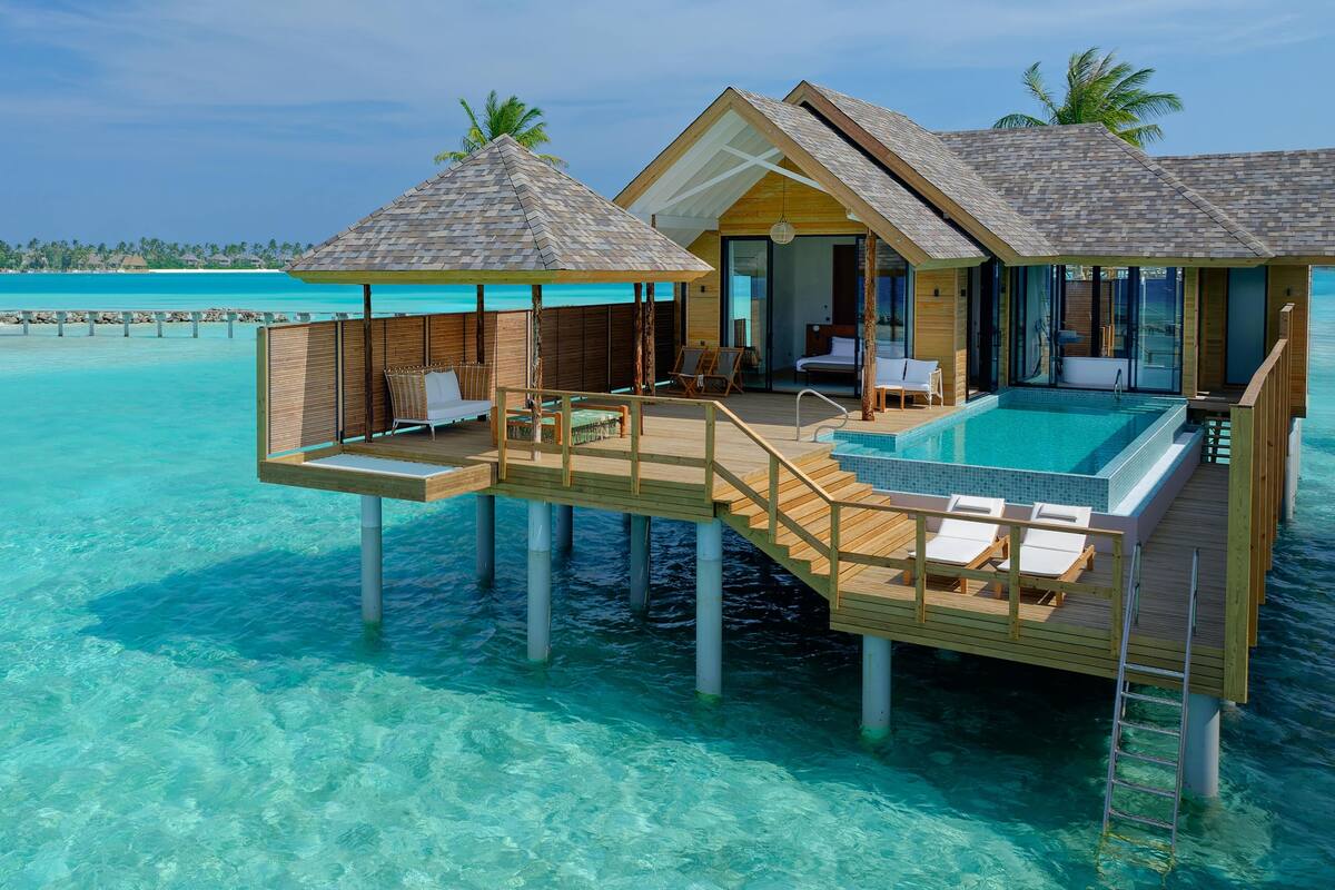 Overwater bungalows with a pool, wooden deck, and lounge chairs.