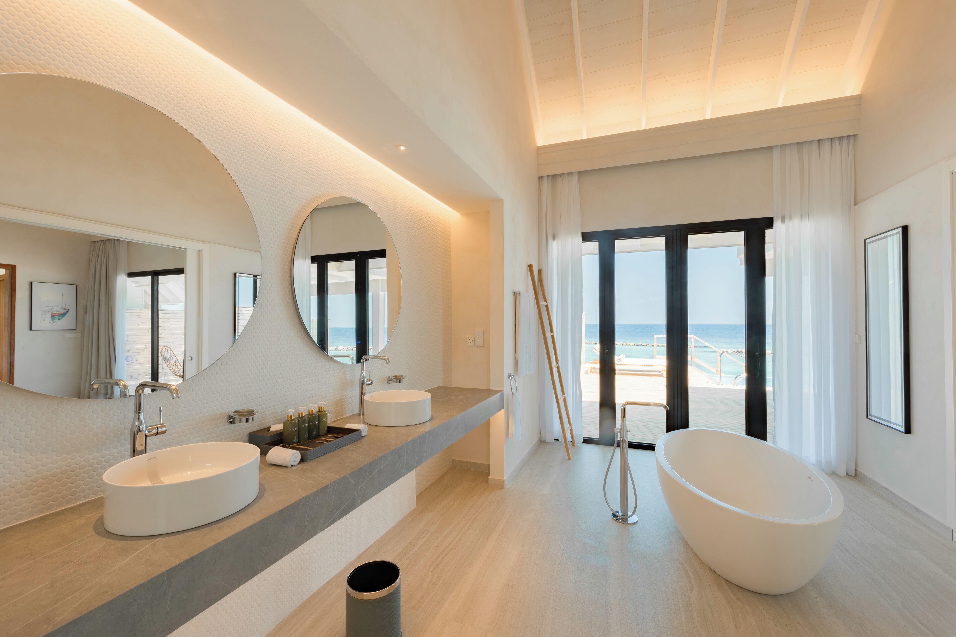Un baño moderno con un lavamanos ovalado grande, una bañera independiente y un espejo amplio.