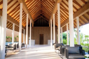 Un espacio al aire libre techado con vigas y columnas de madera, que incluye sofás y sillones.