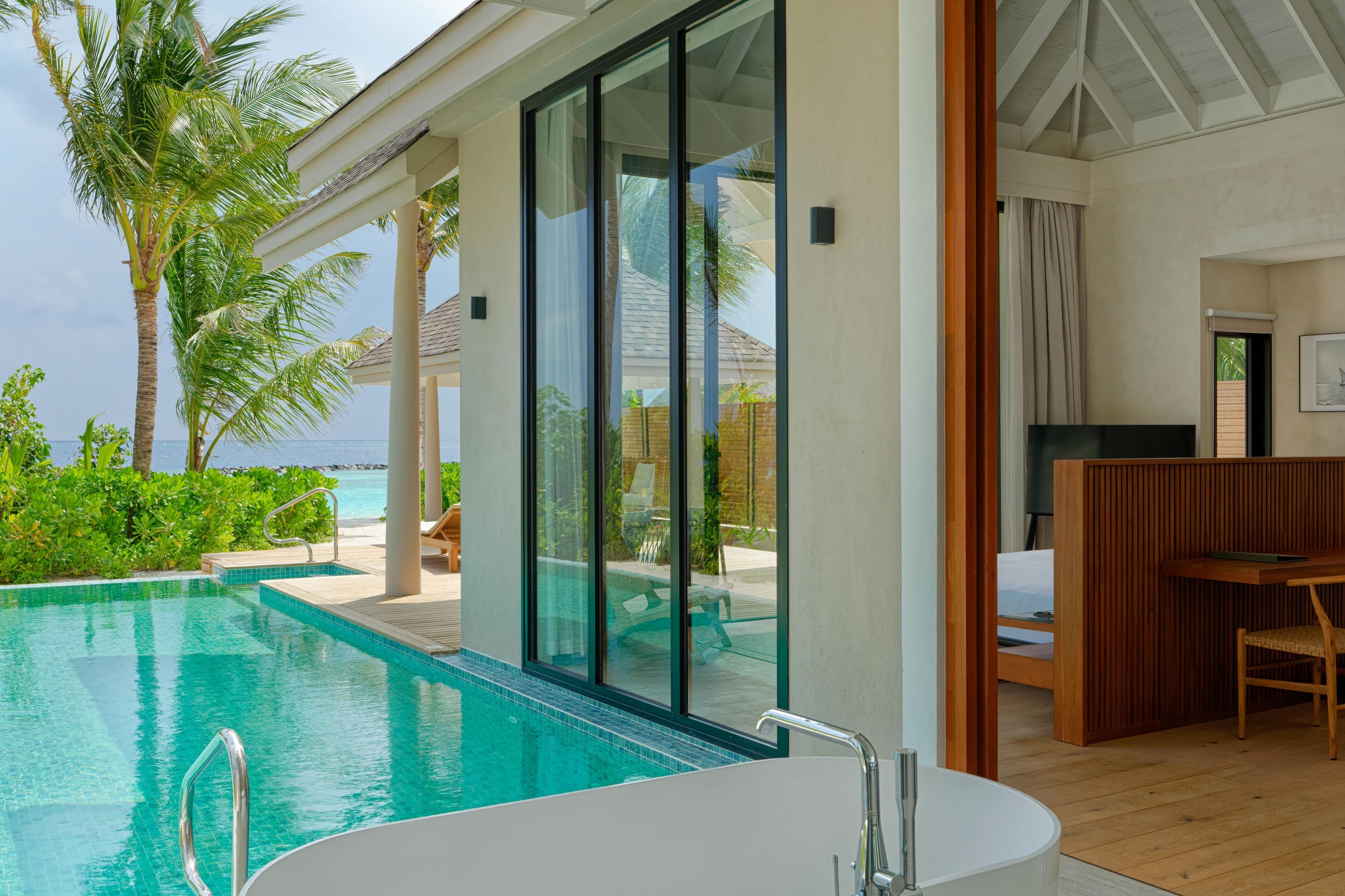 A modern hotel room with a large glass window, a private pool, and a wooden deck.