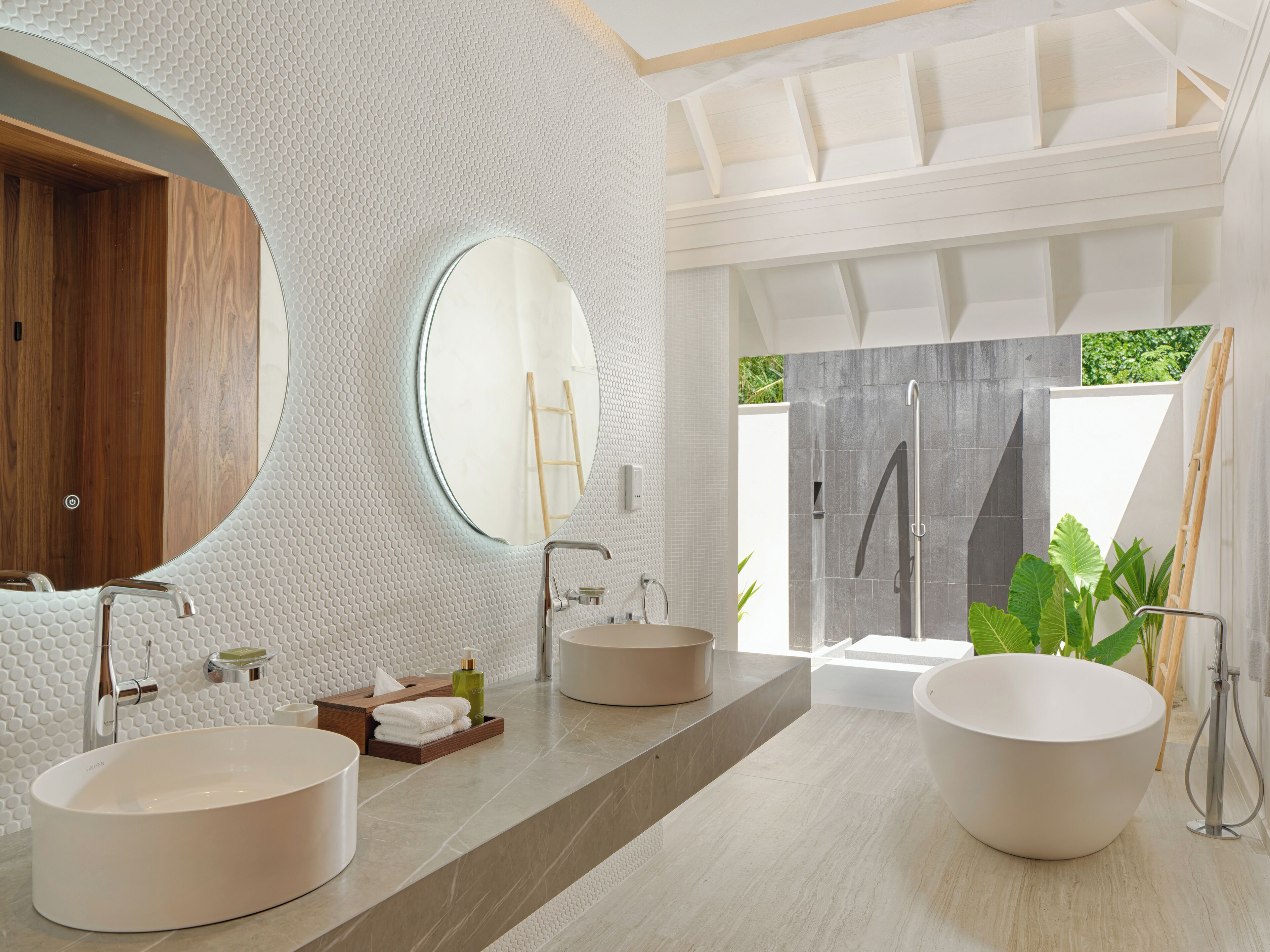A modern bathroom with two large sinks, a round mirror, and a shower area.