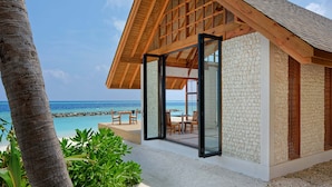 Une maison de plage moderne dotée d’une grande porte vitrée donnant sur un patio aménagé avec du mobilier d’extérieur.