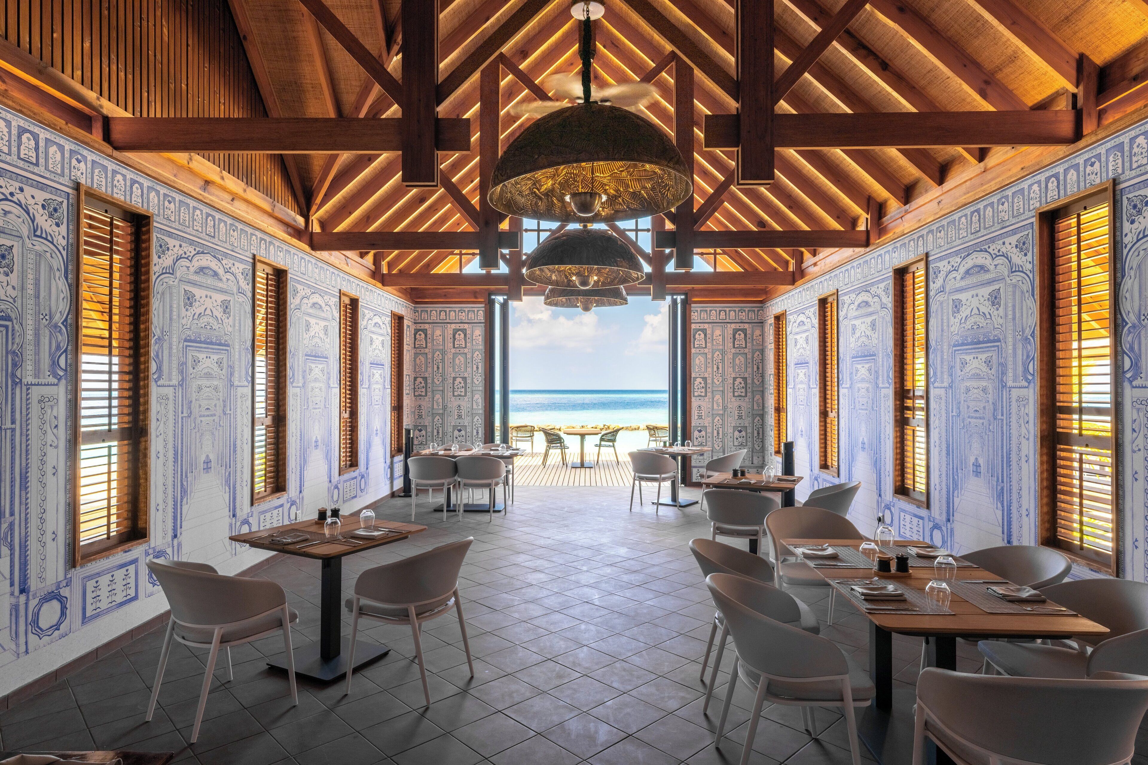 Ristorante con vista sulla spiaggia, caratterizzato da travi in legno, pareti con decorazioni blu e un'arredamento moderno.