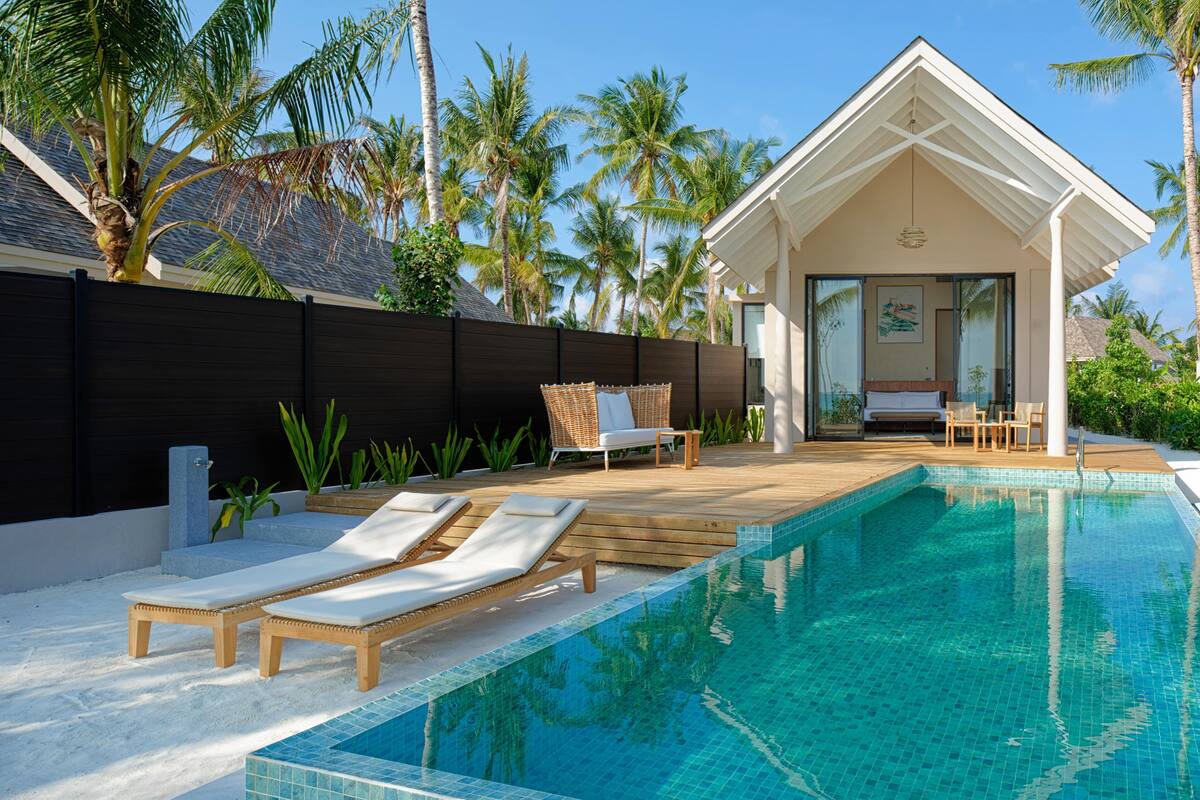 A pool area with lounge chairs, a wooden deck, and a building with a glass door.