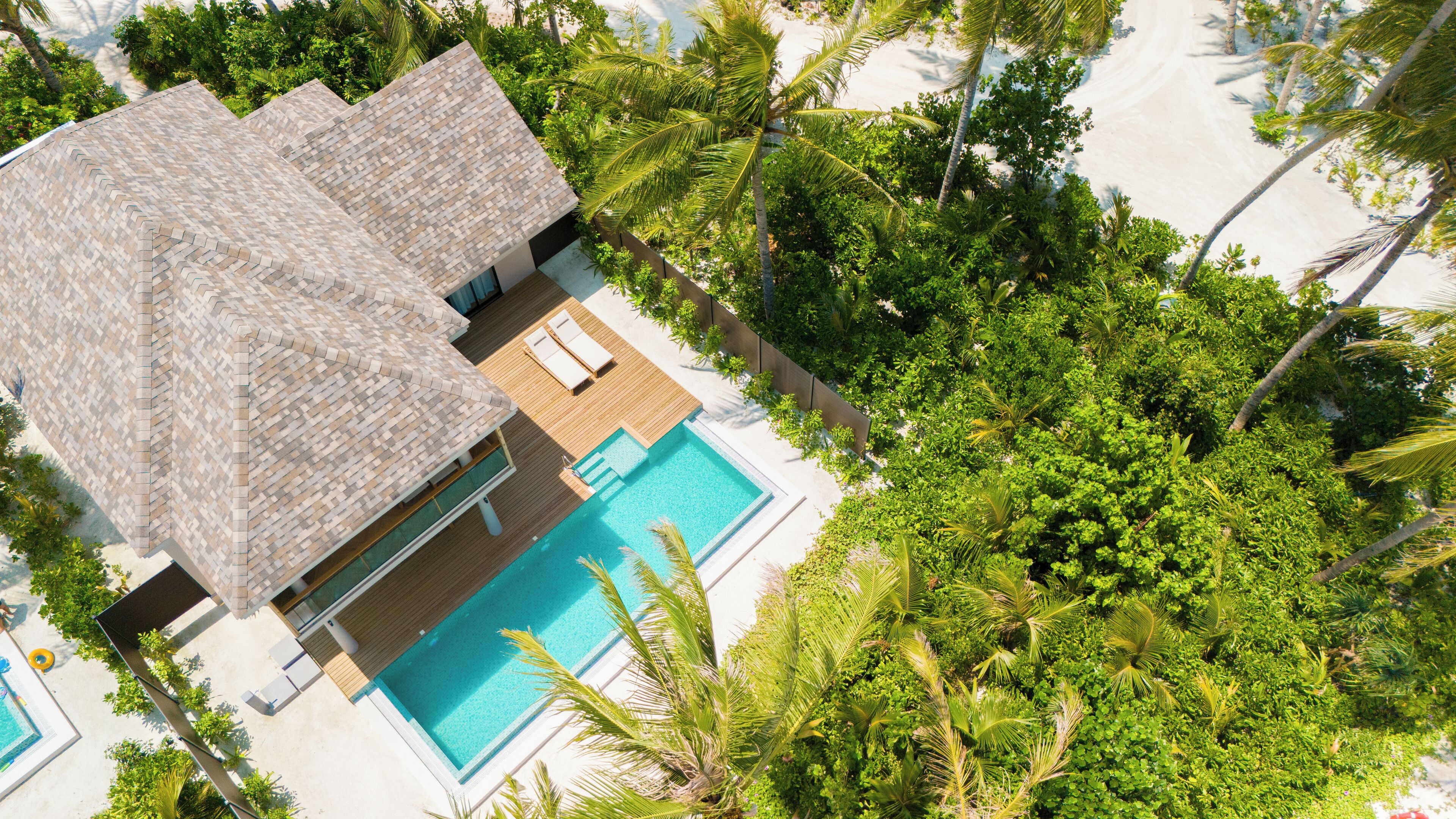 An aerial view of a resort with a swimming pool, a thatched-roof structure, and lush greenery.