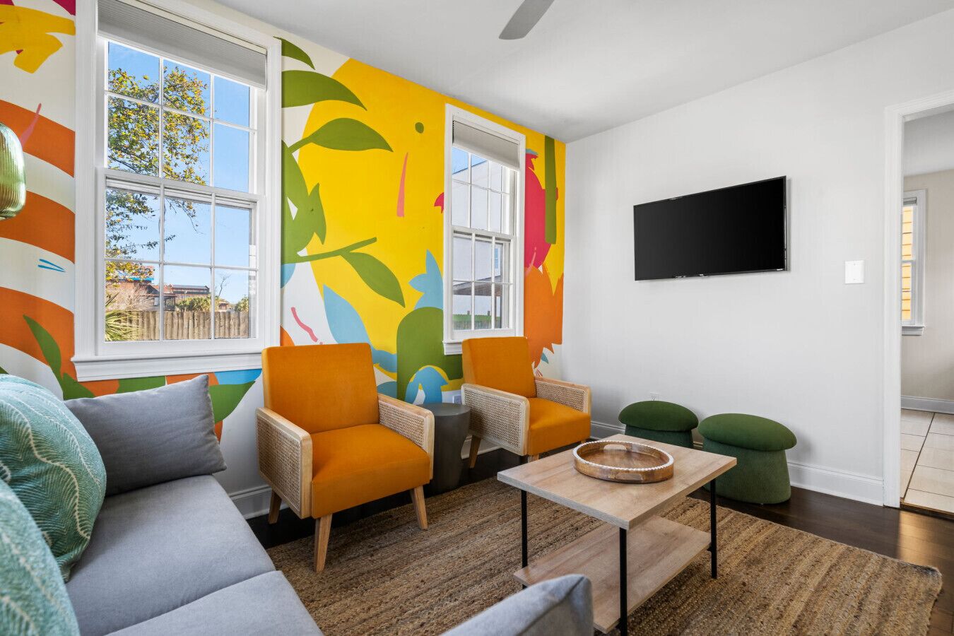 Ein modernes Wohnzimmer mit einem farbenfrohen abstrakten Wandgemälde, zwei orangefarbenen Sesseln, einem grauen Sofa, einem Holztisch und einem flachbildfernseher, der an der Wand montiert ist.