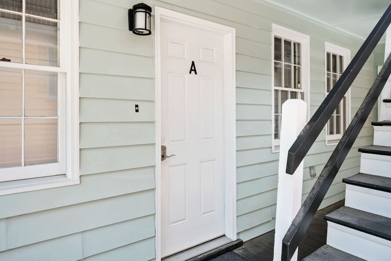 A white door labeled 'A' with a black mailbox, a window with blinds, and a black staircase.
