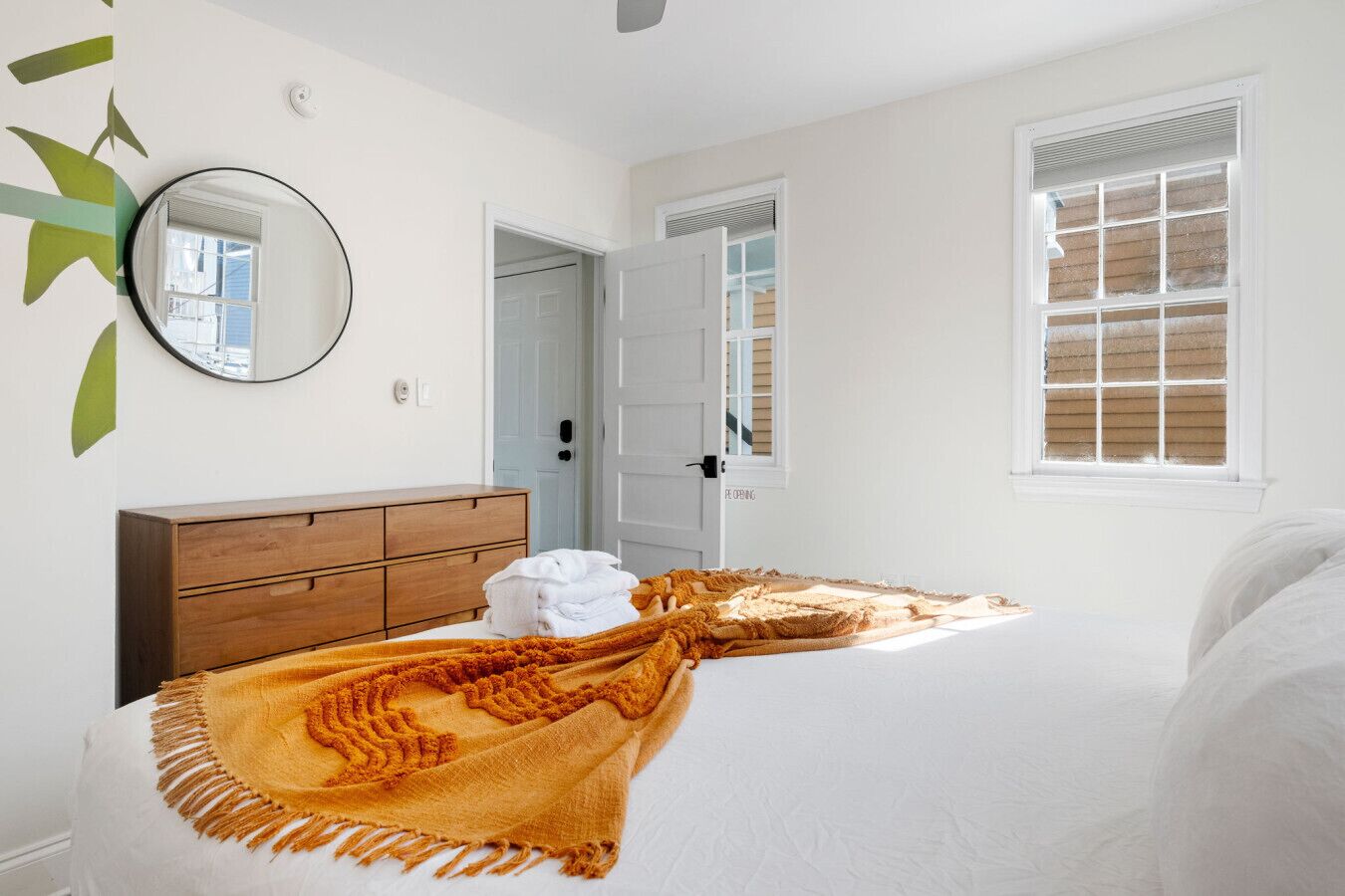 A bedroom with a bed, a wooden dresser, a mirror, and a window with blinds.