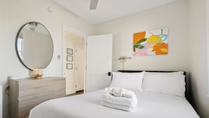 Quarto de hotel com uma cama grande, penteadeira de madeira, espelho redondo e uma pintura abstrata colorida na parede.
