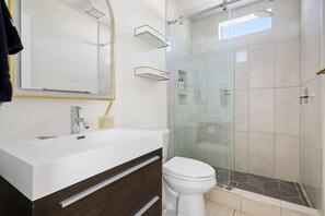 Un baño moderno con tocador blanco, cabina de ducha de vidrio y un espejo grande con marco dorado.