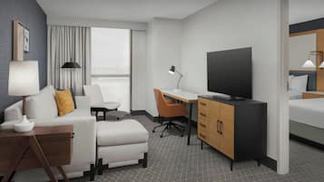 A modern hotel room with a sofa, a desk, a television, and a bed.
