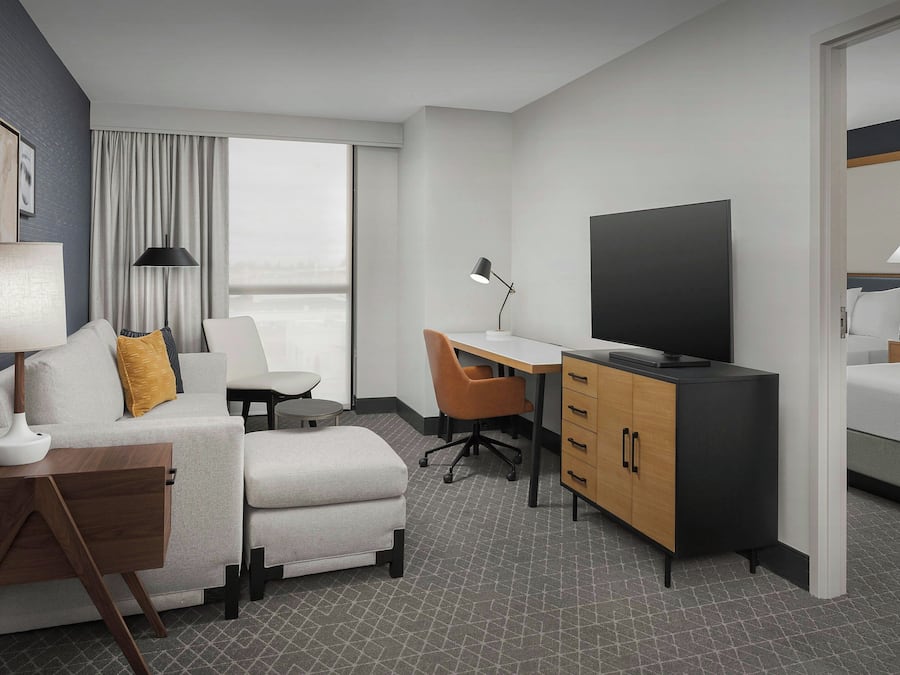 A modern hotel room with a sofa, a desk, a television, and a bed.