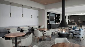 A modern restaurant with round tables and chairs, a central fire feature, and a bar area with a TV. - Residence Inn by Marriott Seattle Northgate Station (Seattle)