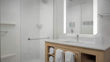 Un baño moderno con cabina de ducha, un espejo grande, un lavabo blanco y un mueble de tocador de madera con estantes.