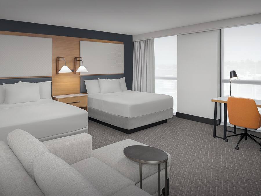 Una habitación de hotel moderna con dos camas, un escritorio, una silla naranja y una pequeña mesa redonda.