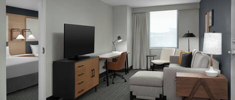 A modern hotel room with a bed, a desk, a television, a sofa, and a window with curtains.