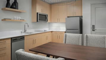 A modern kitchen with wooden cabinets, a built-in microwave, a stainless steel refrigerator, and a dining table with four chairs.