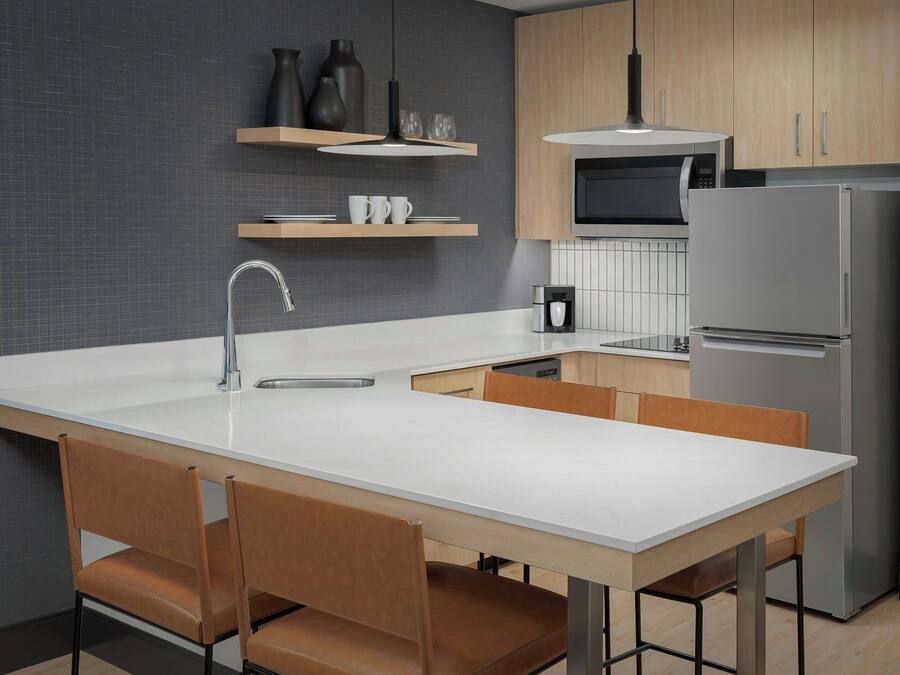 A modern kitchen with a white countertop, stainless steel appliances, and wooden chairs.