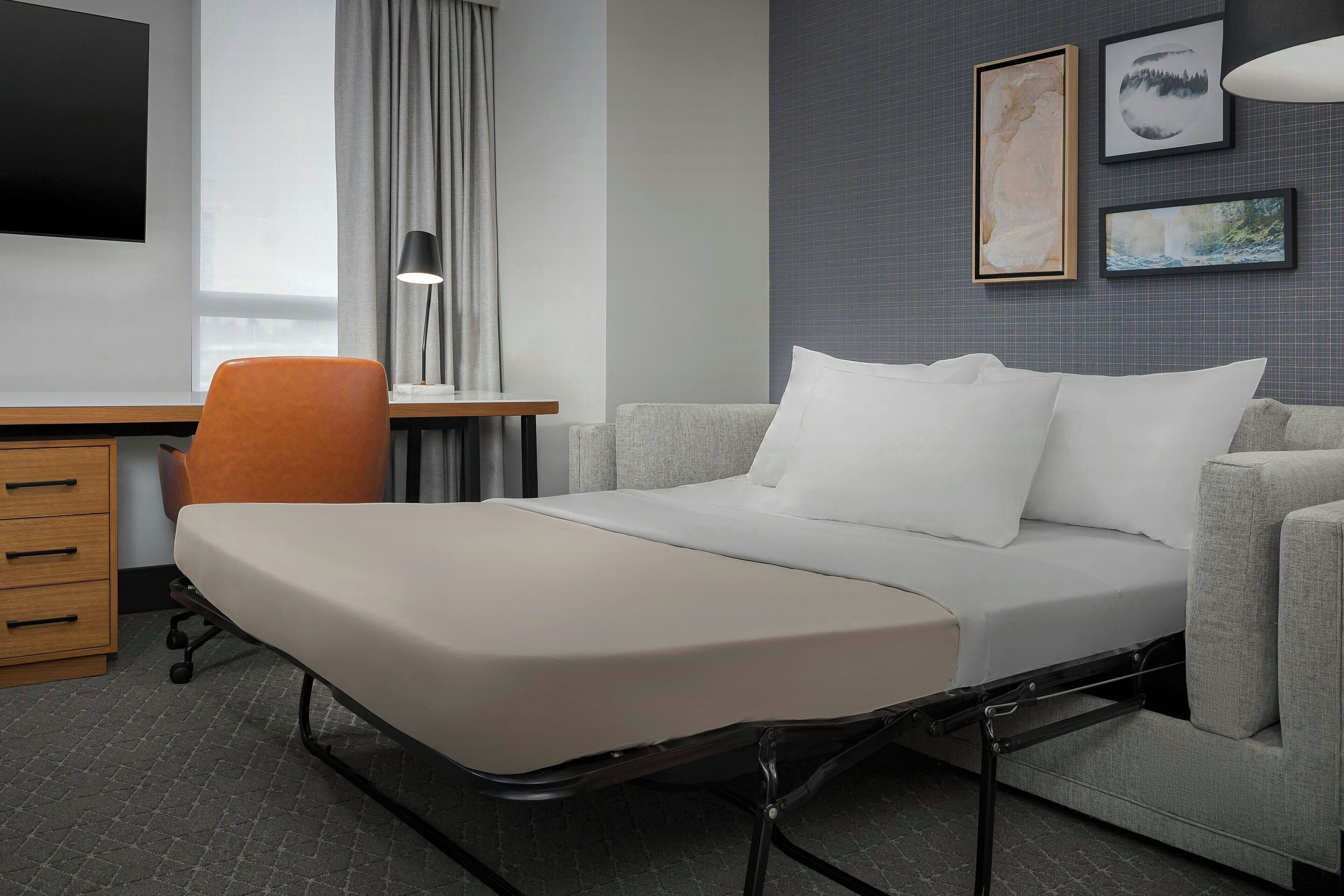 A modern hotel room with a bed, a desk, a chair, and a TV.