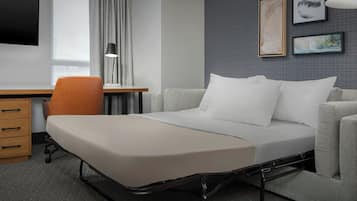A modern hotel room with a bed, a desk, a chair, and a TV.