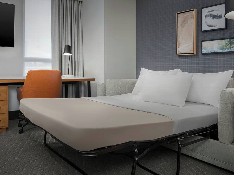 Una habitación de hotel moderna con una cama, un escritorio, una silla y un televisor.