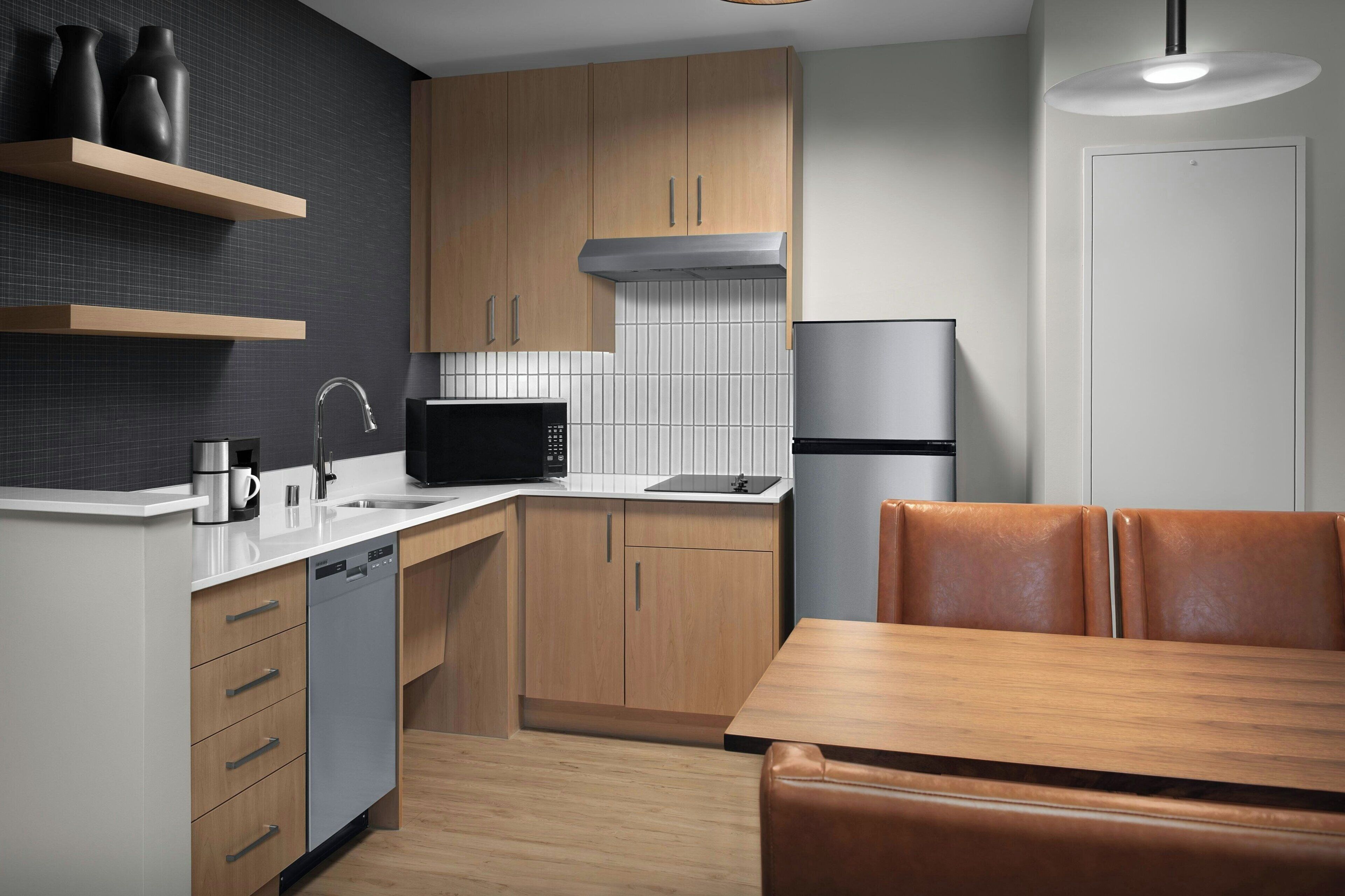 A modern kitchen with wooden cabinets, a stainless steel dishwasher, a black microwave, and a refrigerator.