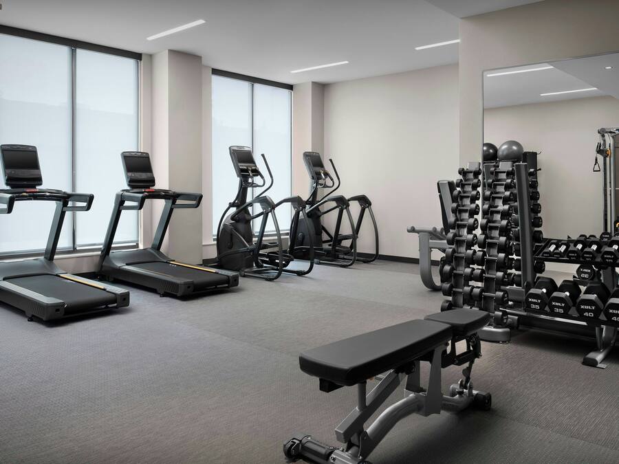 A gym with treadmills, elliptical machines, a bench, and weightlifting equipment.
