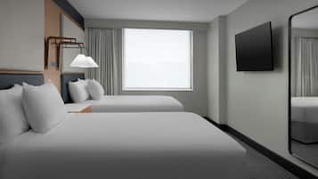 Quarto de hotel com duas camas, uma janela grande, uma TV de tela plana e um espelho.