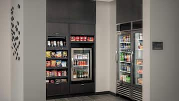 Un área de cocina moderna con un refrigerador lleno de bebidas y aperitivos, un microondas y una cafetera.