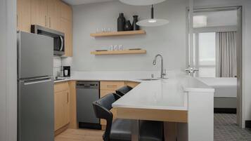 A modern kitchen with a refrigerator, microwave, and dishwasher, wooden cabinets, and a dining area with a white countertop and black chairs.