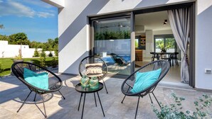 Une terrasse extérieure moderne, dotée de deux fauteuils en osier, d’une petite table ronde et d’une porte vitrée donnant sur un espace intérieur.