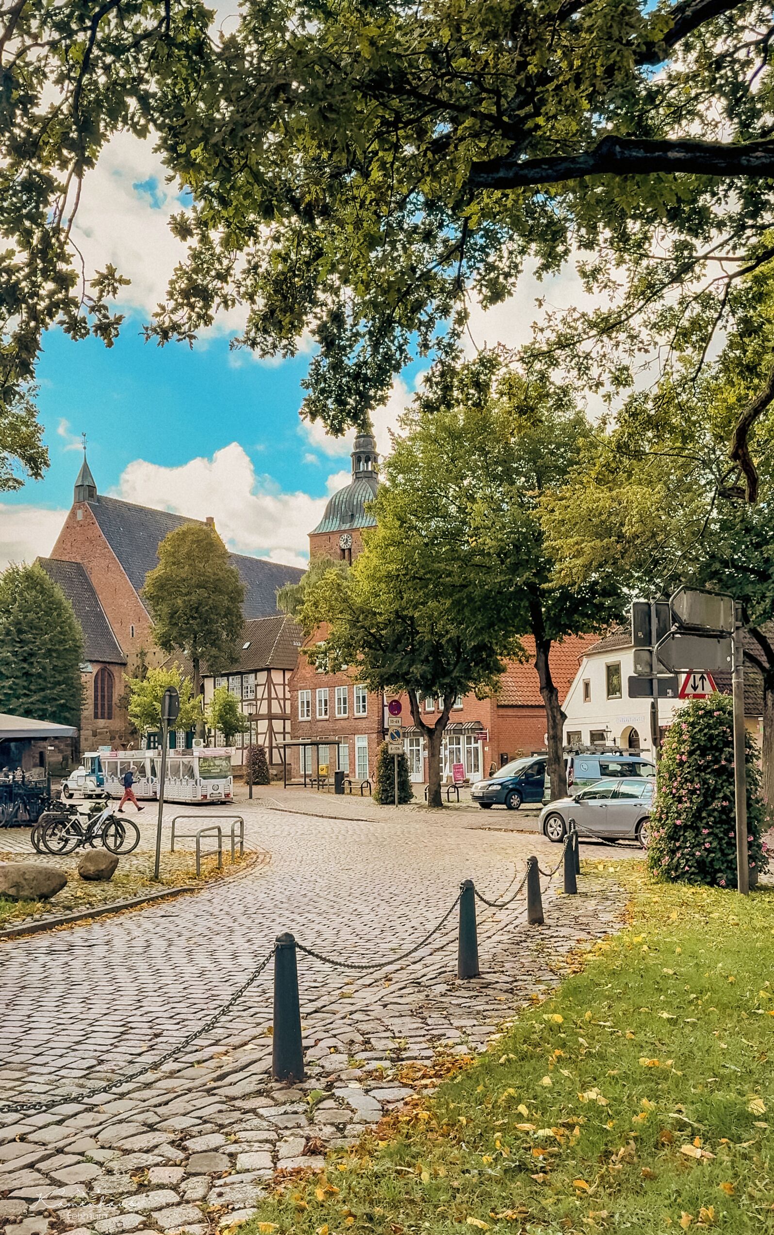 A cobblestone street with historic buildings, a church tower, and a clear sky.