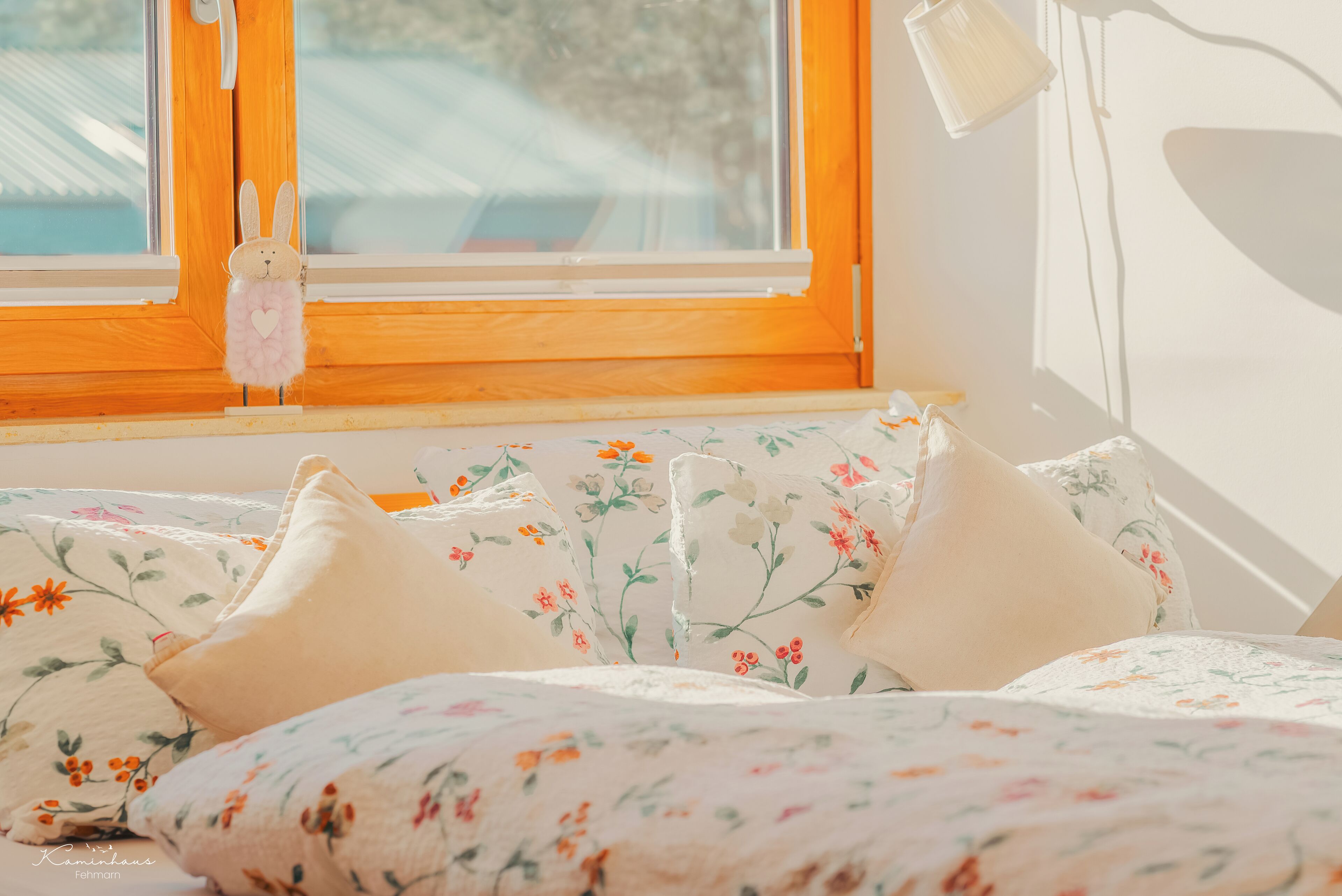 A bed with floral bedding and a window with a wooden frame and a hanging decoration.