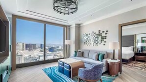 Ein modernes Hotelzimmer mit weitreichendem Stadtblick, einer Couch, einem Sessel, einem Nachttisch und einer Lampe.