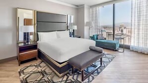 Ein modernes Hotelzimmer mit einem großen Bett, einer Bank, einem Nachttisch, einer Lampe, Blick auf die Stadt und einem großen Fenster.