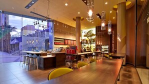 Ein modernes Café-Interieur mit einem langen Holztisch, gelben Stühlen und einer Bar mit Hockern.