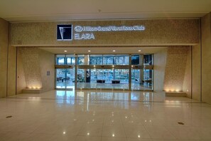 Eine geräumige Lobby mit Glastür, einem Schild für Hilton Grand Vacations Club ELARA und freiem Blick nach draußen.
