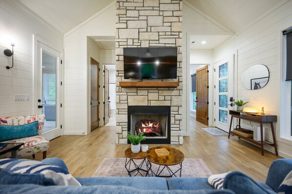 Una sala de estar con chimenea de piedra, un televisor de pantalla plana montado encima y un rincón de estar acogedor con un sofá y una mesa de centro.
