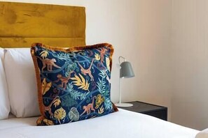 Een bed met een wit kussen en een sierkussen met een tropisch ontwerp.