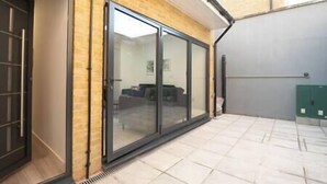 A modern building with a large sliding glass door leading to an outdoor area with a tiled floor. - PBC | Studio Apt in Richmond (RICH3) (London)