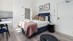 A modern bedroom with a bed, bedside table, and a small round table. - PBC | Studio Apt in Richmond (RICH3) (London)