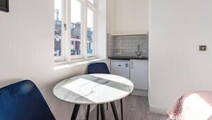 A compact kitchen with a window, a small dining table, and a chair. - PBC | Studio Apt in Richmond (RICH3) (London)