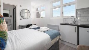Une chambre d’hôtel moderne équipée d’un lit, d’un petit bureau, d’un miroir et d’une kitchenette.