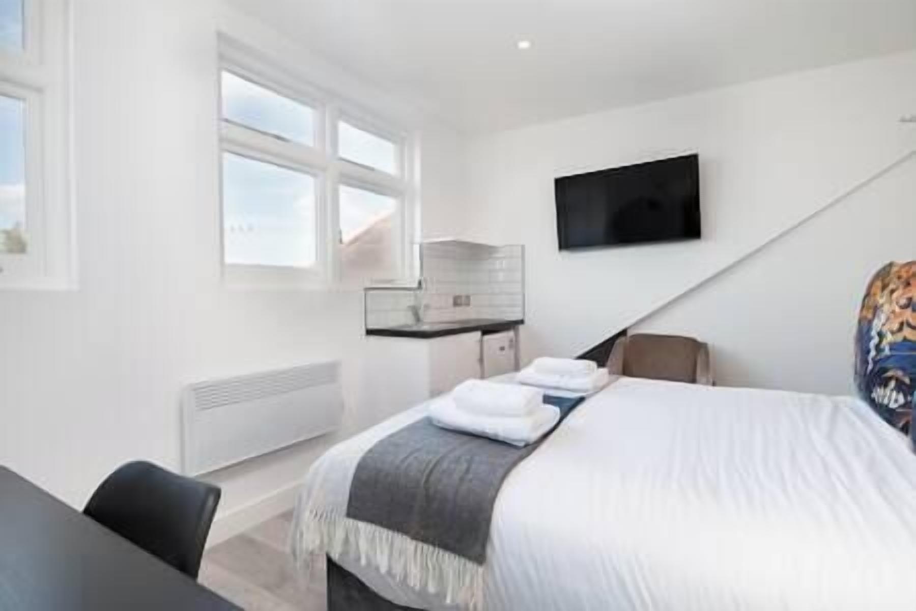 Une chambre d’hôtel moderne dotée d’un grand lit, d’un bureau avec un ordinateur, d’un téléviseur fixé au mur et d’une fenêtre offrant une vue sur le ciel.